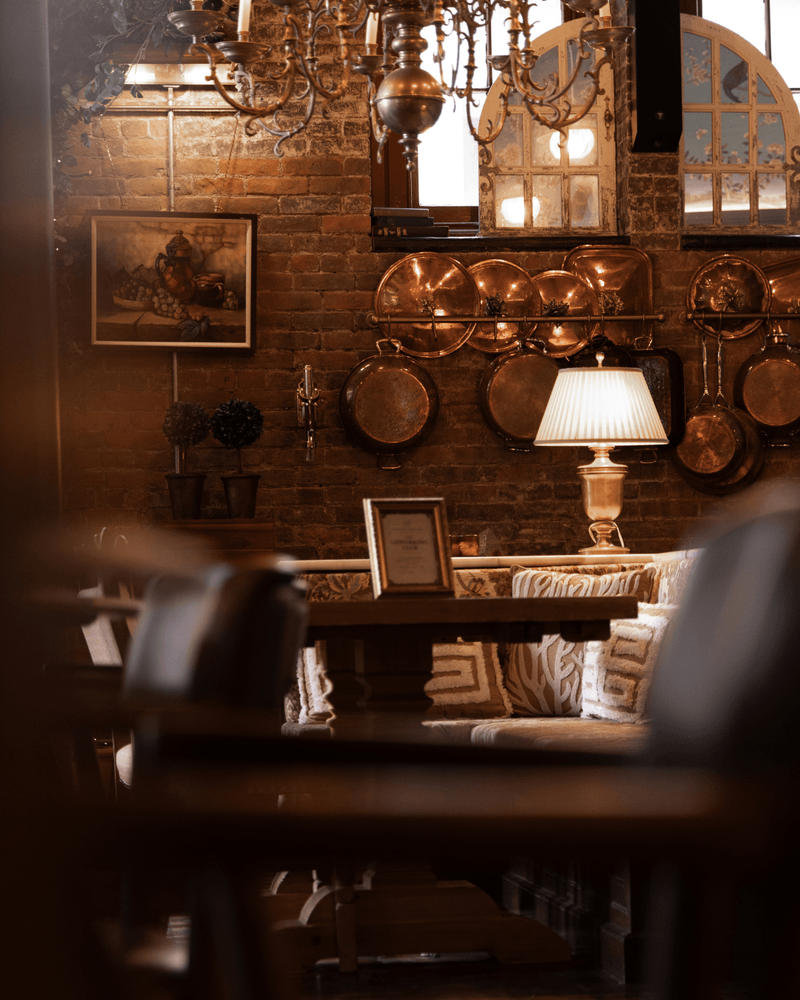 Copper pans catch the light from Visual Comfort’s table lamp, while mirrored panels and brick lend warmth and texture.