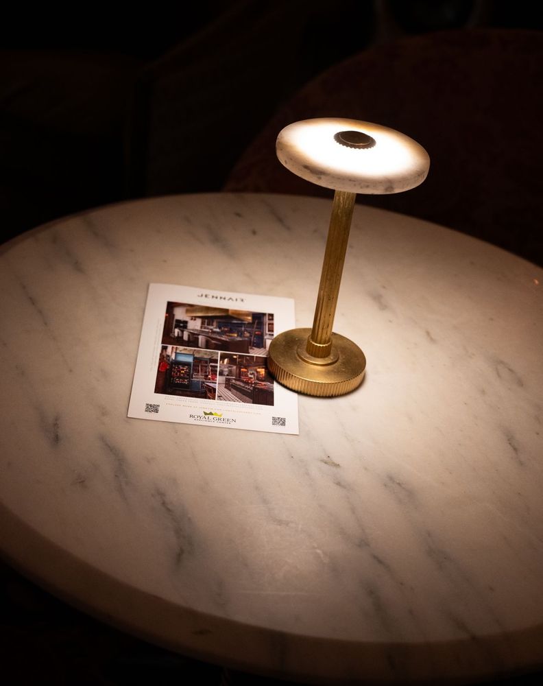 A brass table lamp casts direct light across a smooth tabletop, drawing focus to printed material during an evening at Maxwell.