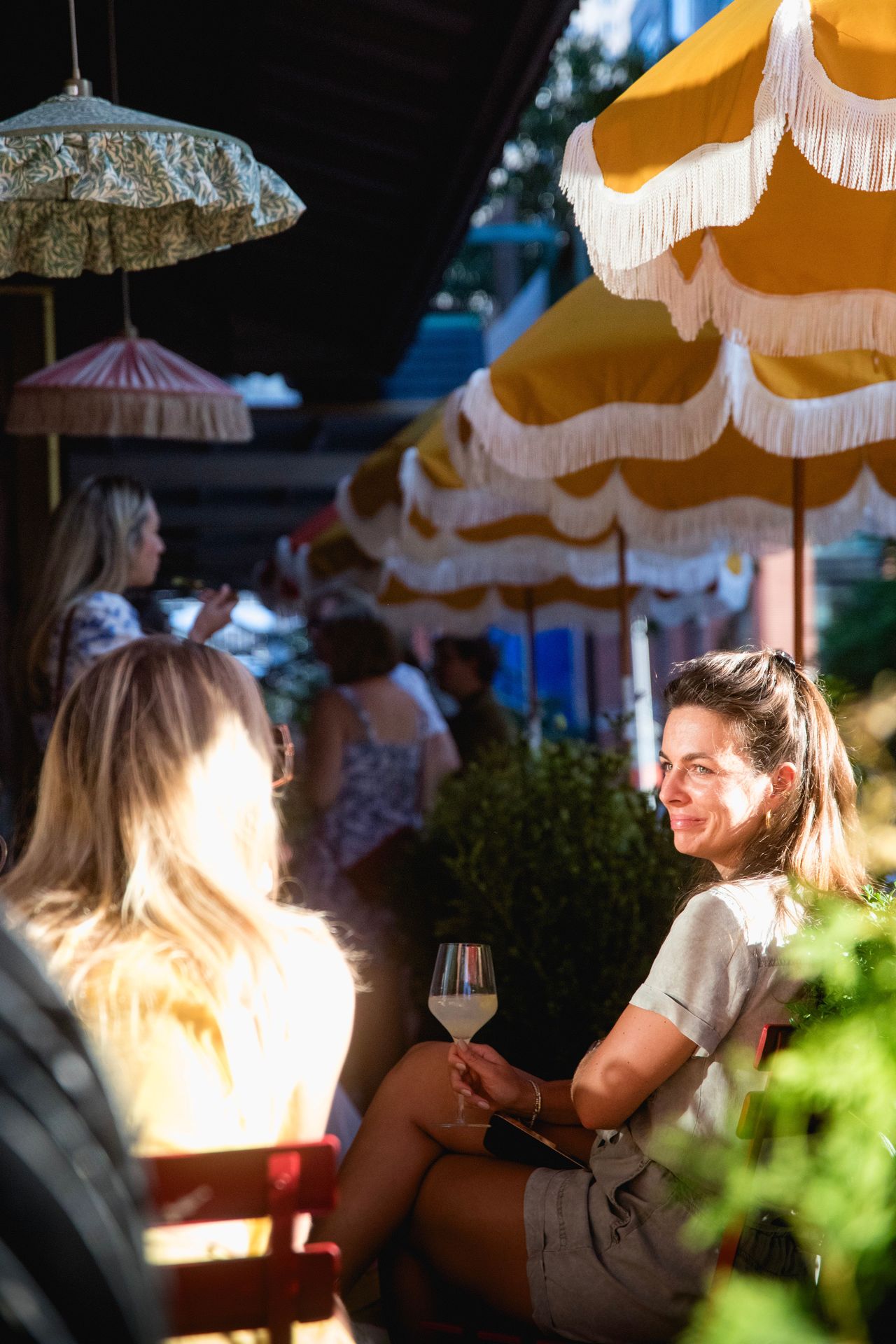 Golden hour at Maxwell when guests gather under striped umbrellas with cocktails in hand as sunlight spills across the sidewalk.