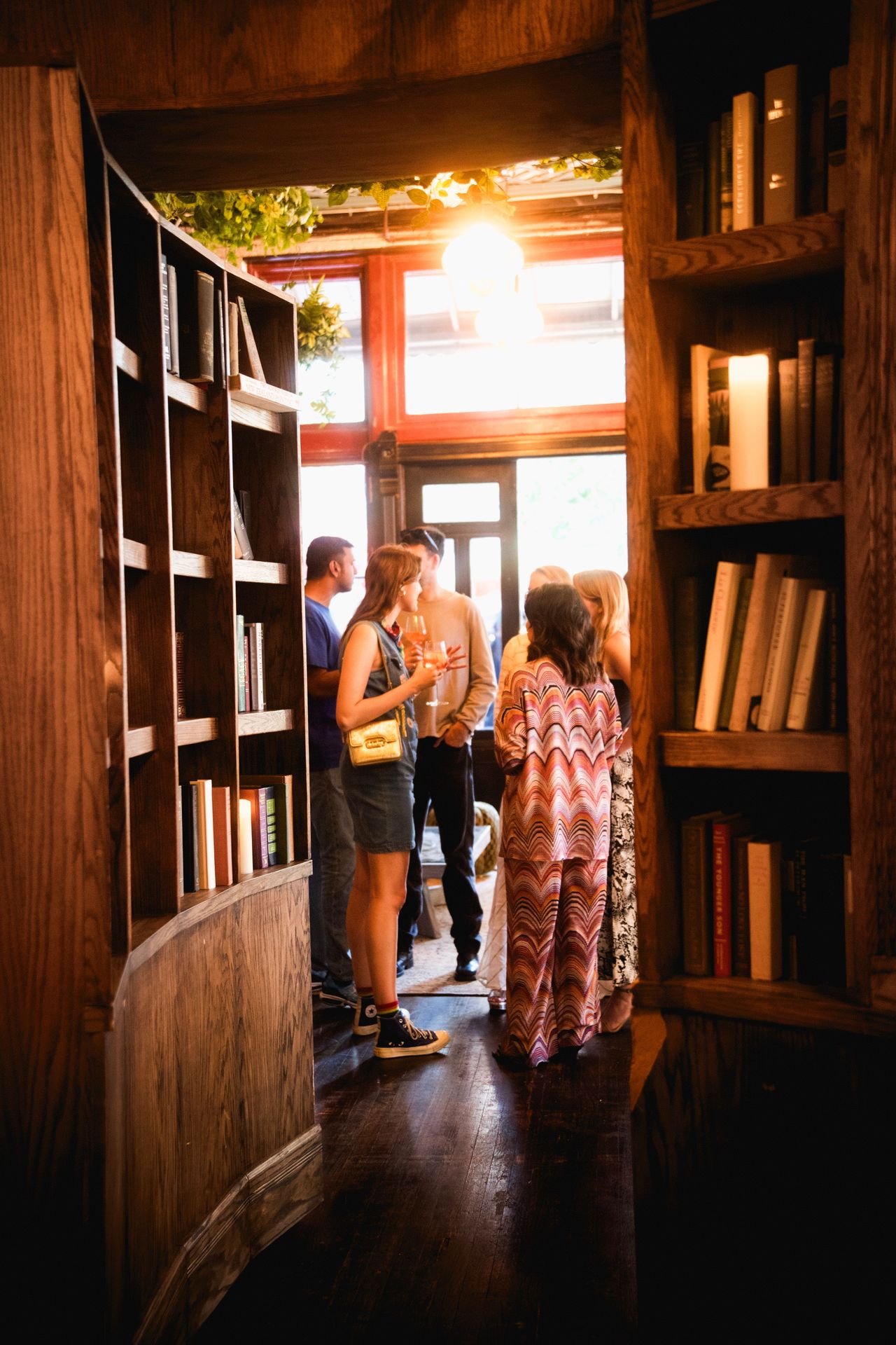 Through the library doorway, guests mingling as the golden hour light spills inside