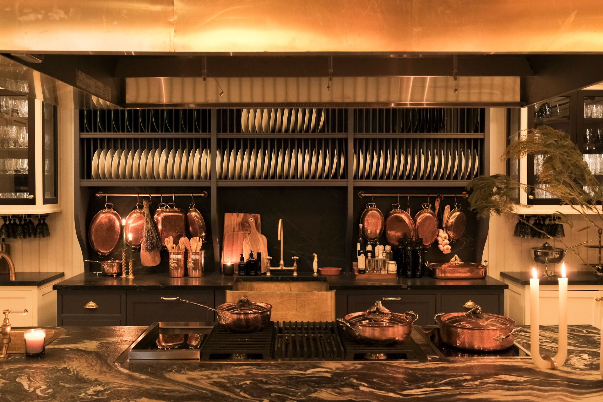Maxwell’s Grand Kitchen featuring a marble island, copper Ruffoni pots, plate rack, and black and brass detailing.