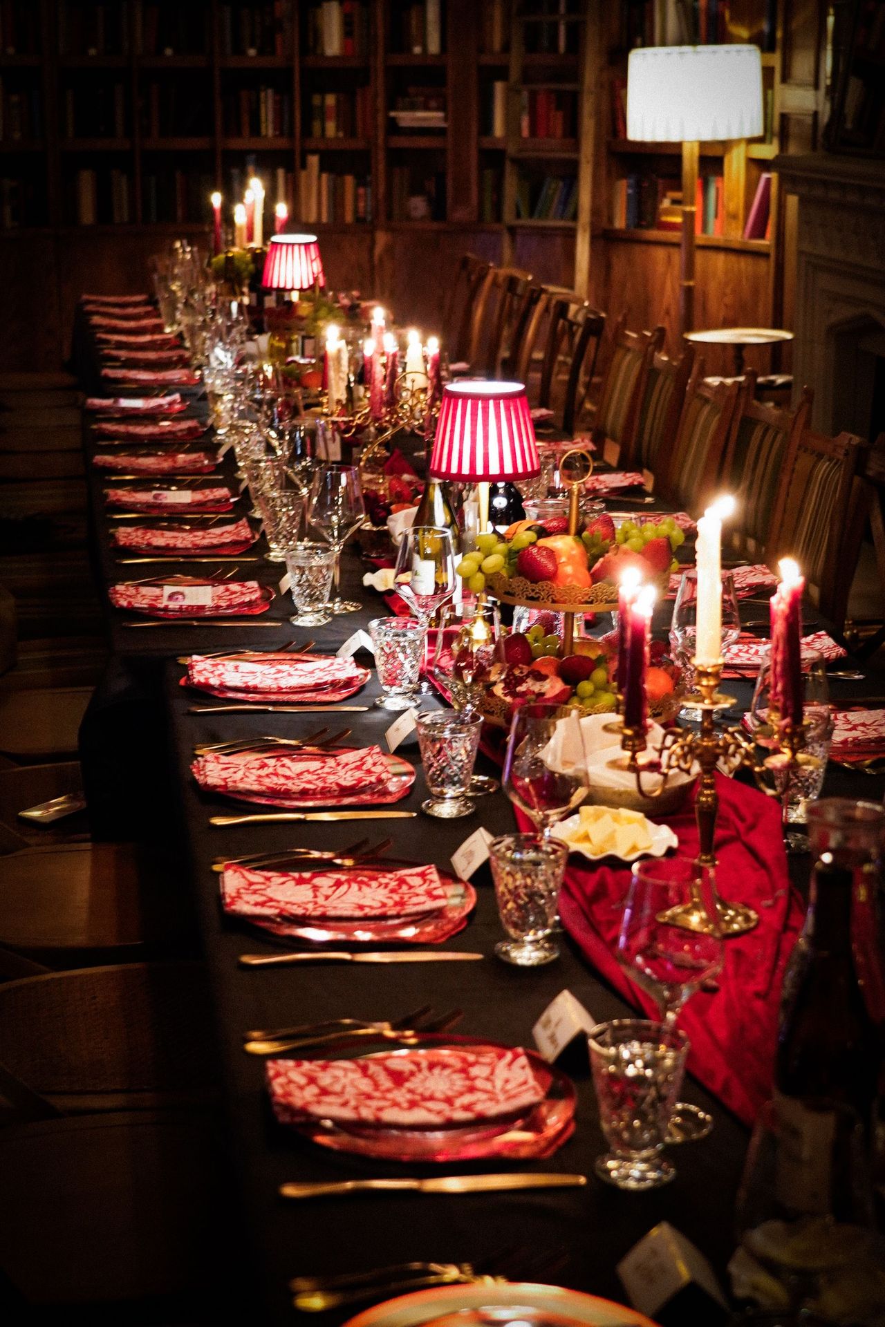 A long table dressed in deep reds and candlelight, ready to host the evening’s gathering