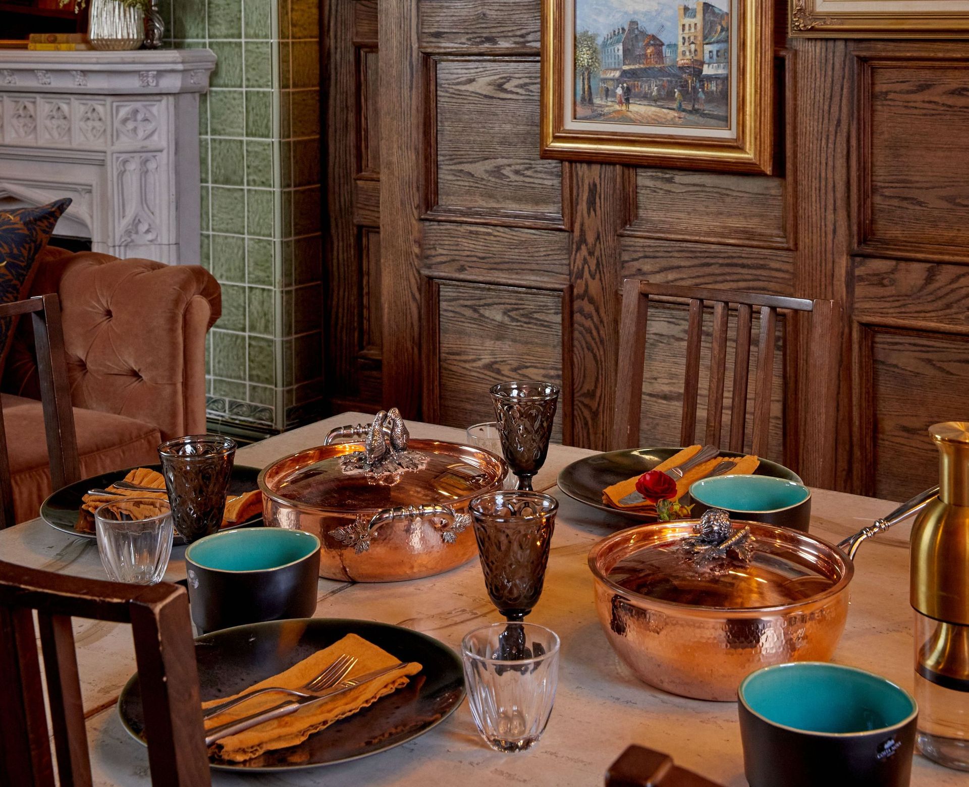 Rustic wood dining table with colorful ceramics, amber glassware, and Ruffoni pots in the center.