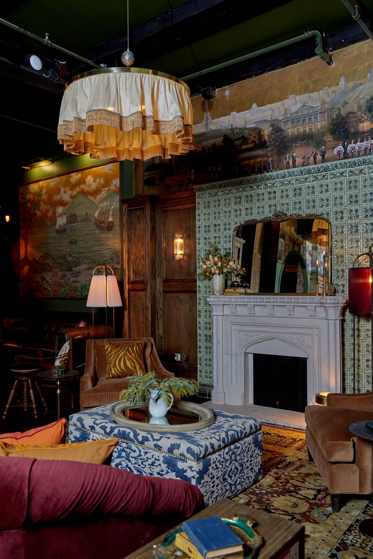 From any angle, the fireplace remains central surrounded by mixed seating, detailed paneling, and painted wall scenes