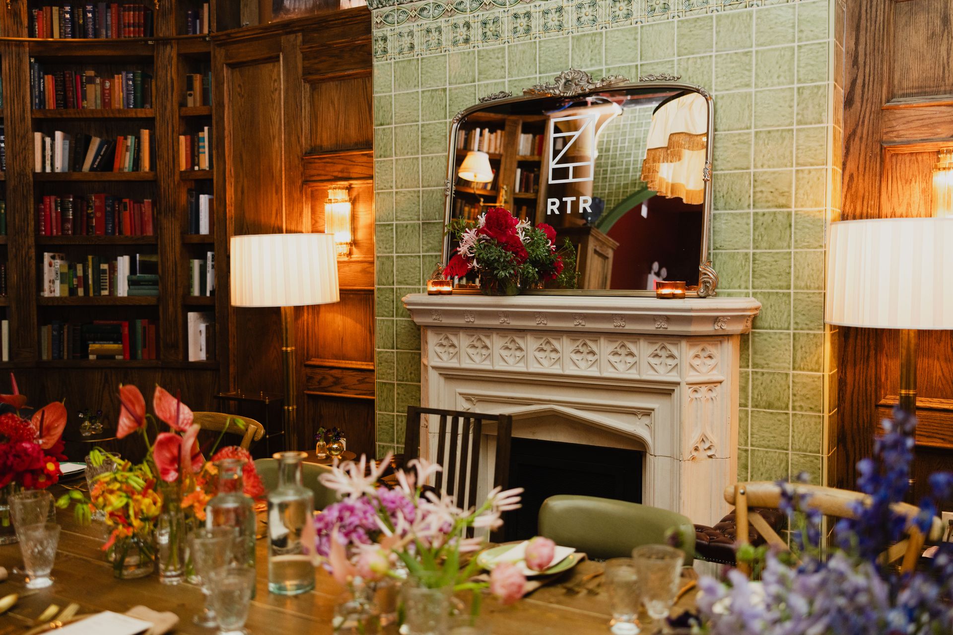 The fireplace with the RTR logo reflected in the mirror above the fireplace, surrounded by fresh flowers and warm lighting